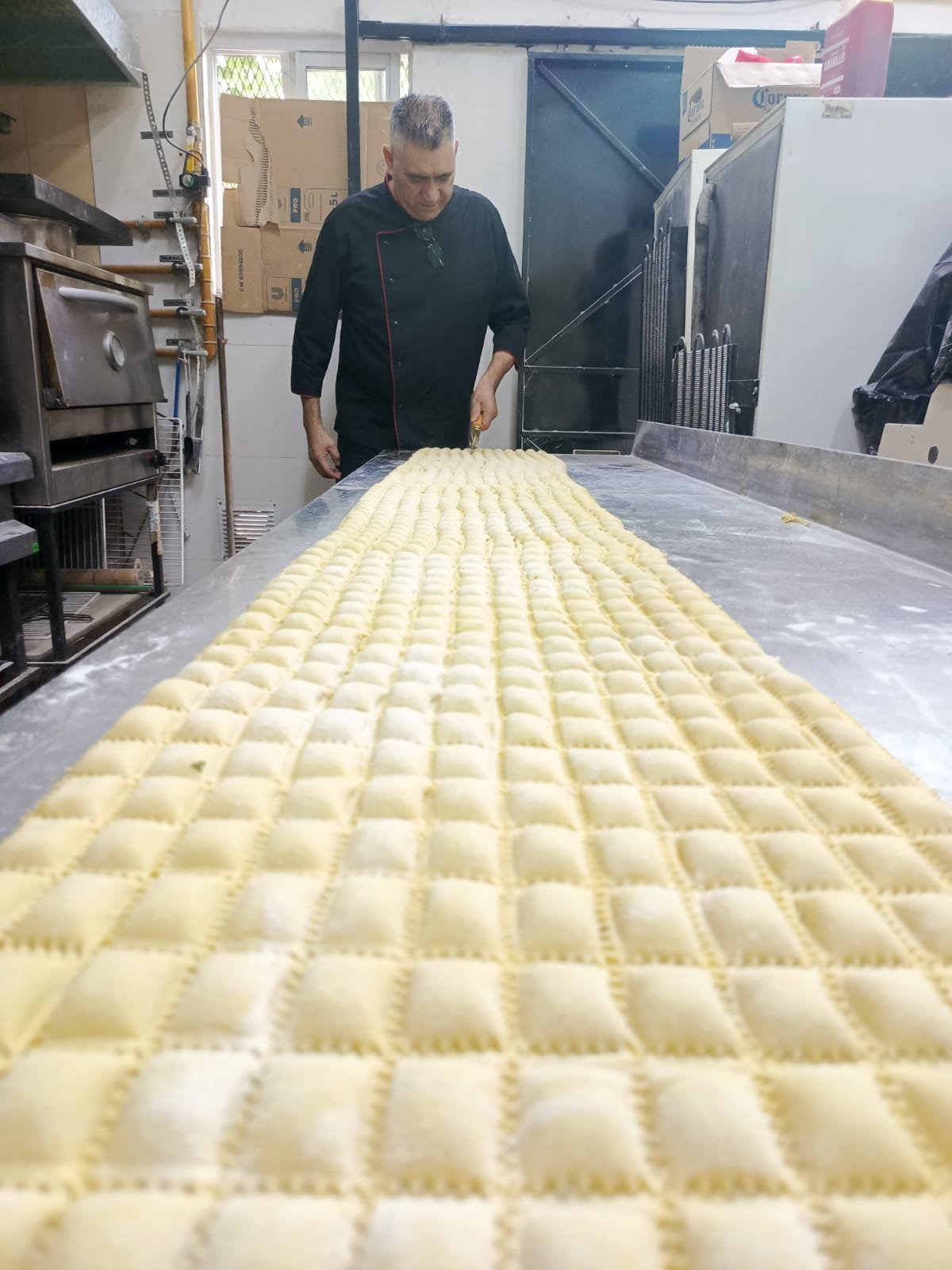 Baker inspecting freshly made pasta sheets arranged in rows on a table in a commercial kitchen.