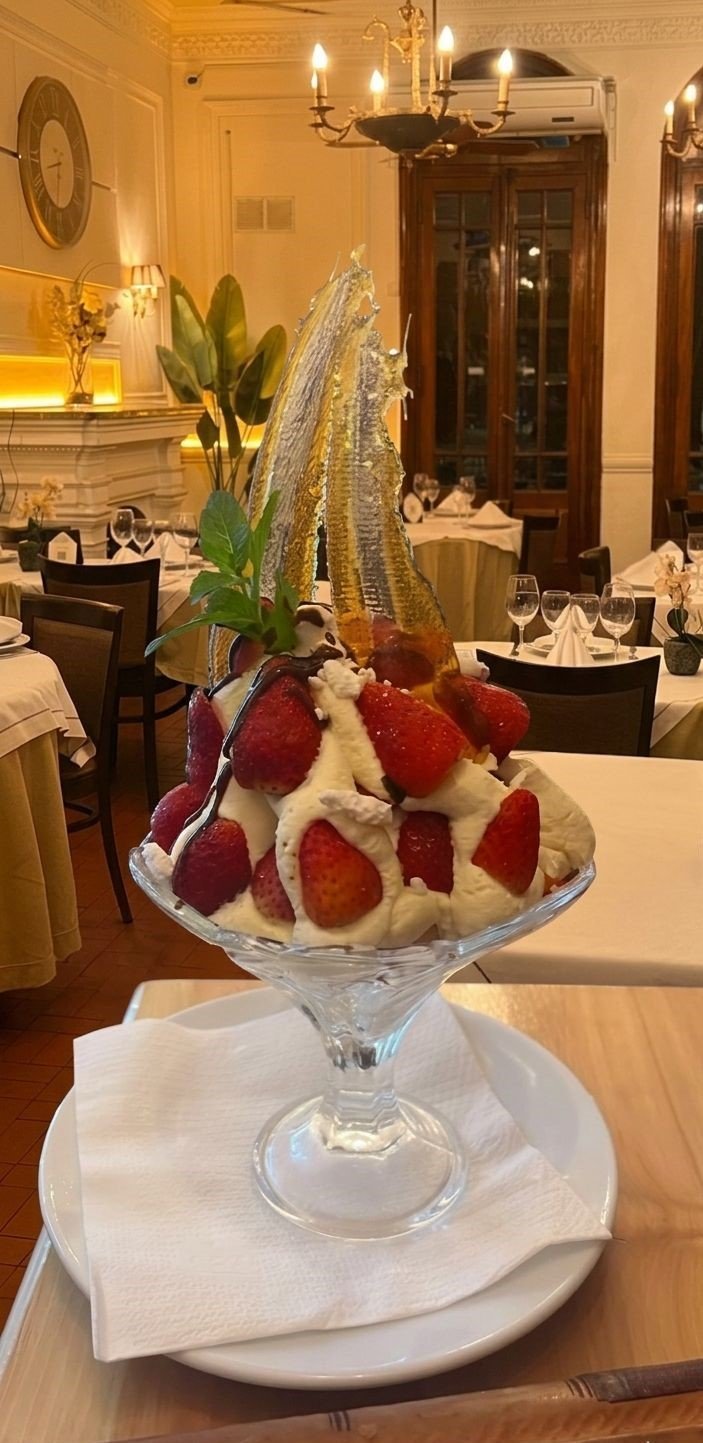Elegant dessert in crystal martini glass with whipped cream and fresh strawberries topped with gold leaf