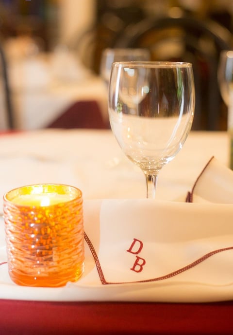 Fine dining table setting with empty wine glass, orange candle, and monogrammed napkin with DB initials
